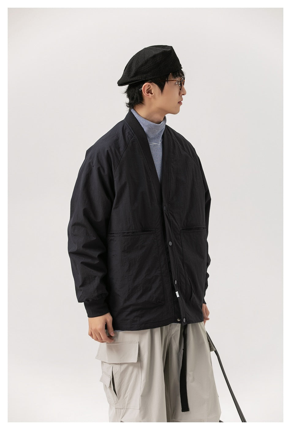 Side view of a model wearing a black snap-front jacket with two large front pockets and light cargo pants.