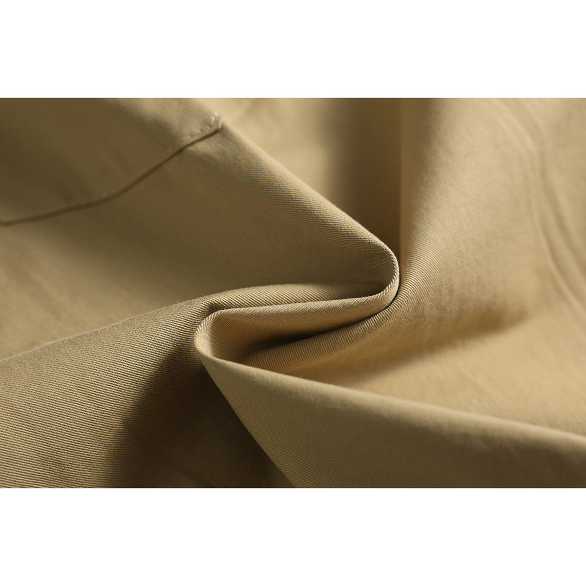 Close-up of tan shorts fabric draped into folds, showing its fine diagonal weave and stitching.