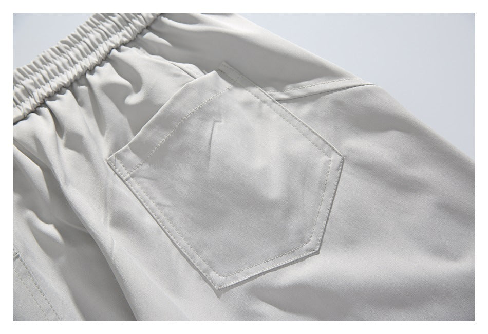 Close-up of light gray pants showing an elastic waistband and a stitched back pocket.
