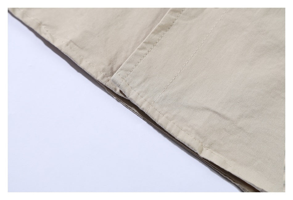 Close-up of the stitched hem and edge of a light khaki garment against a white background.