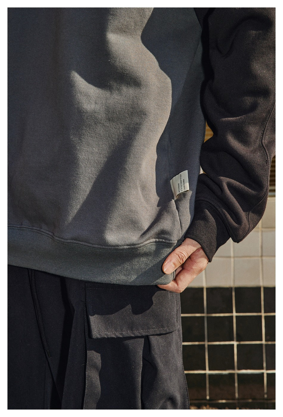 Close-up of a charcoal and black raglan sweatshirt's hem, sleeve, and small side label on a model.