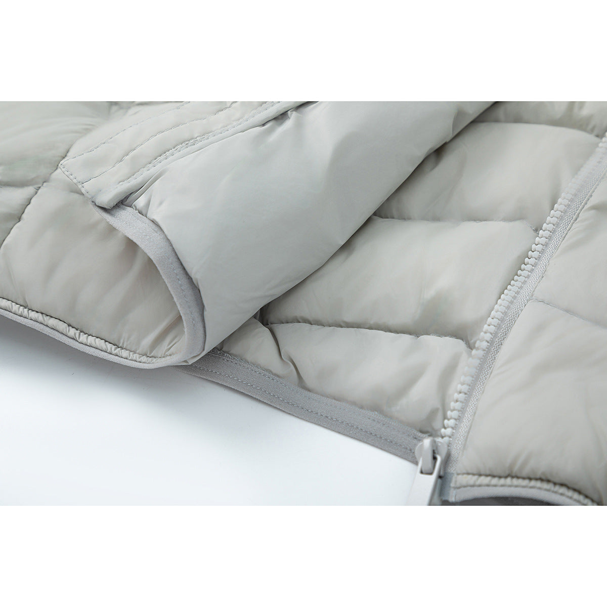 Close-up of a light gray padded jacket showing quilted panels, stitching, and a front zipper.