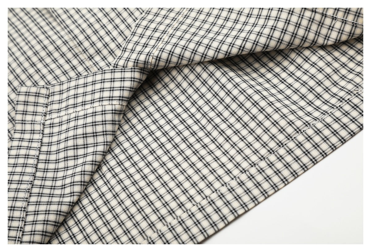 Close-up of stitched seams and folded panels on the cream-and-black plaid shirt.