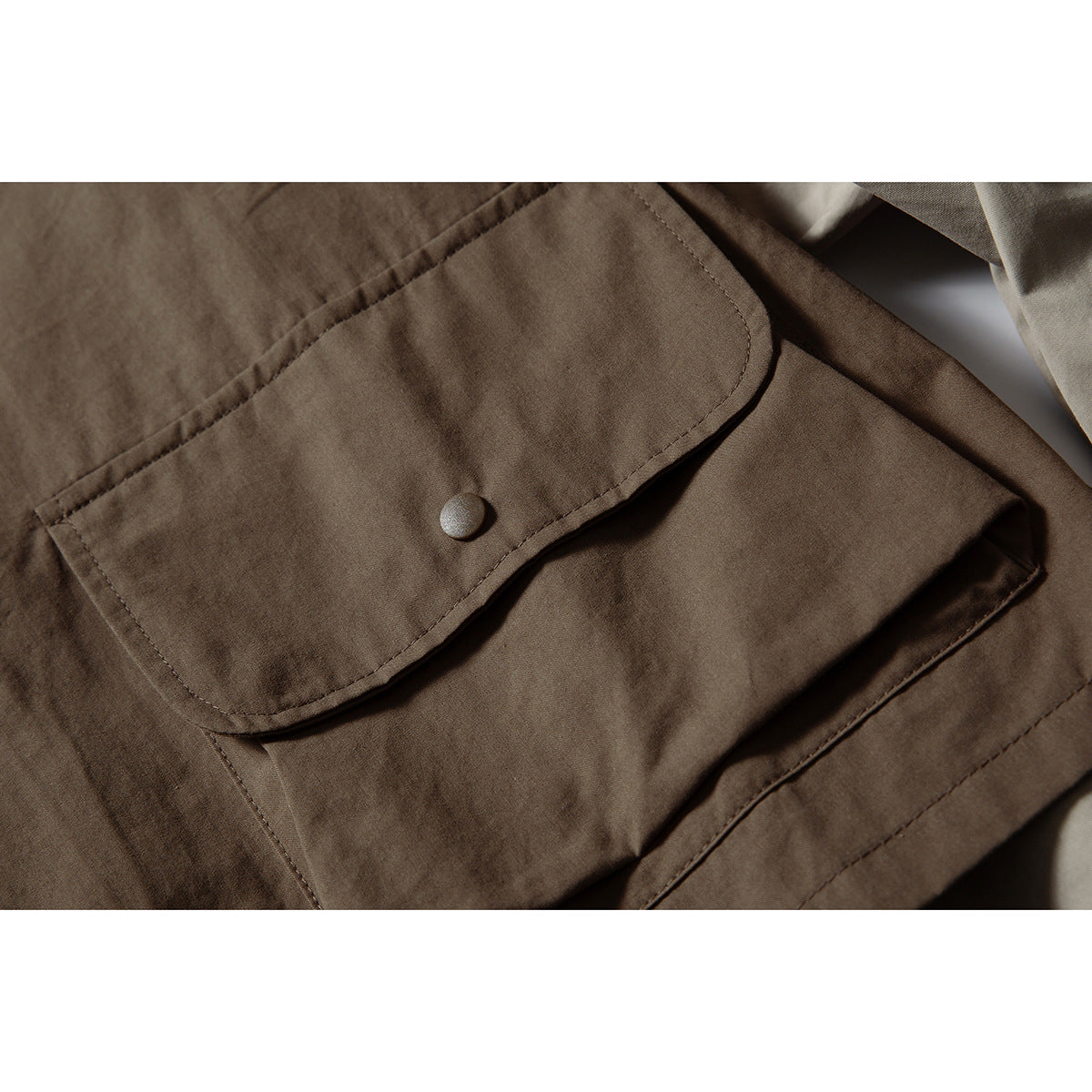 Close-up of a brown garment's large stitched flap pocket with a single snap button.