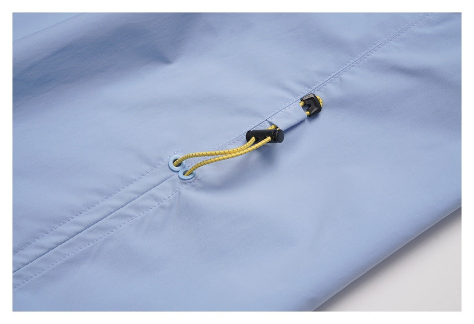 Close-up of light blue garment fabric with a yellow elastic cord and black toggle beside stitched seams.