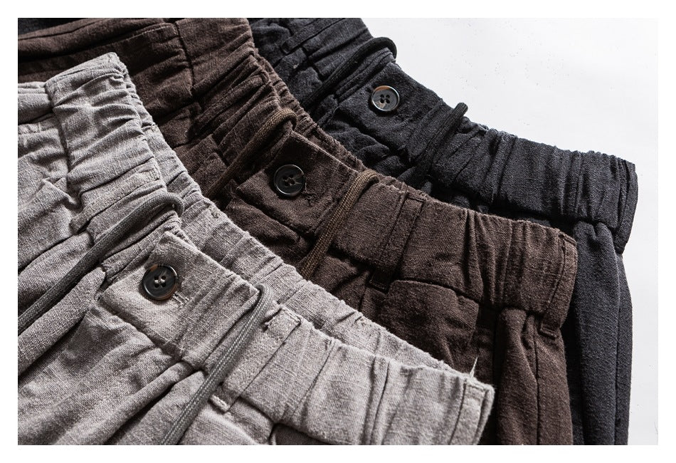 Close-up of elastic-waist trousers in light gray, dark brown, and black, showing buttoned waist tabs.