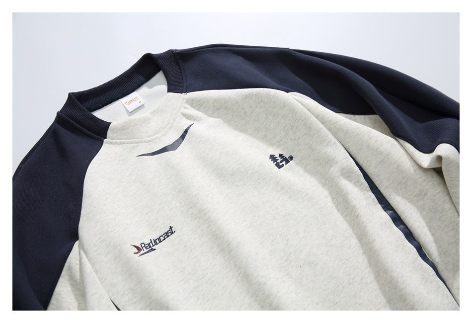 Close-up of the ivory sweatshirt front showing navy sleeve panels, small chest graphics, and collar details.