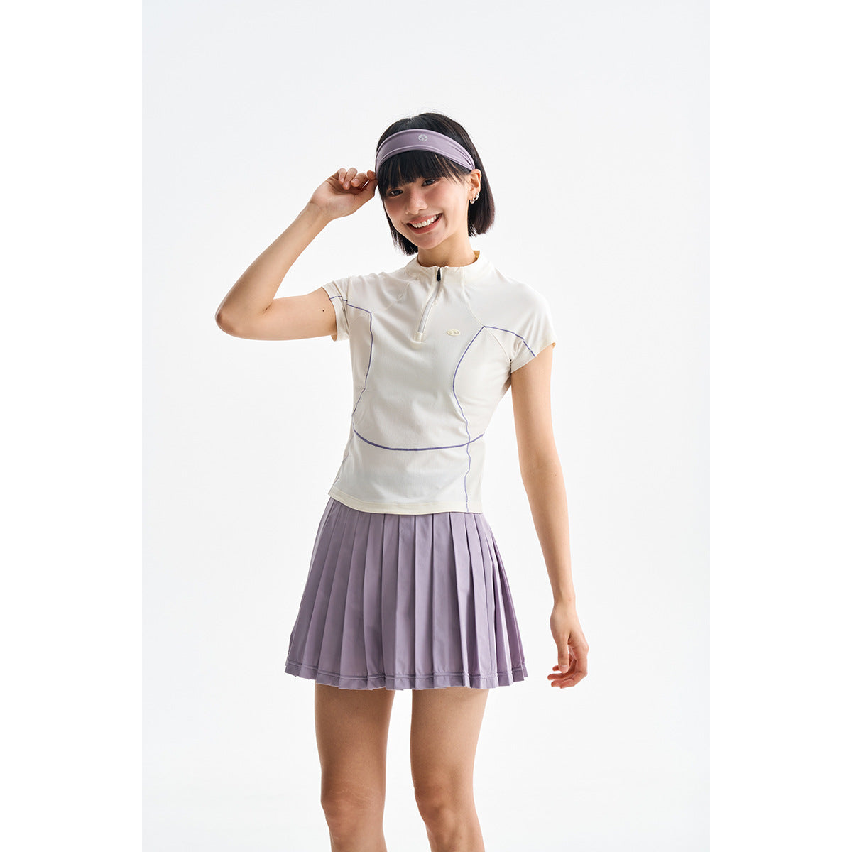 Model wearing an ivory quarter-zip top with purple piping and a lavender pleated skirt.