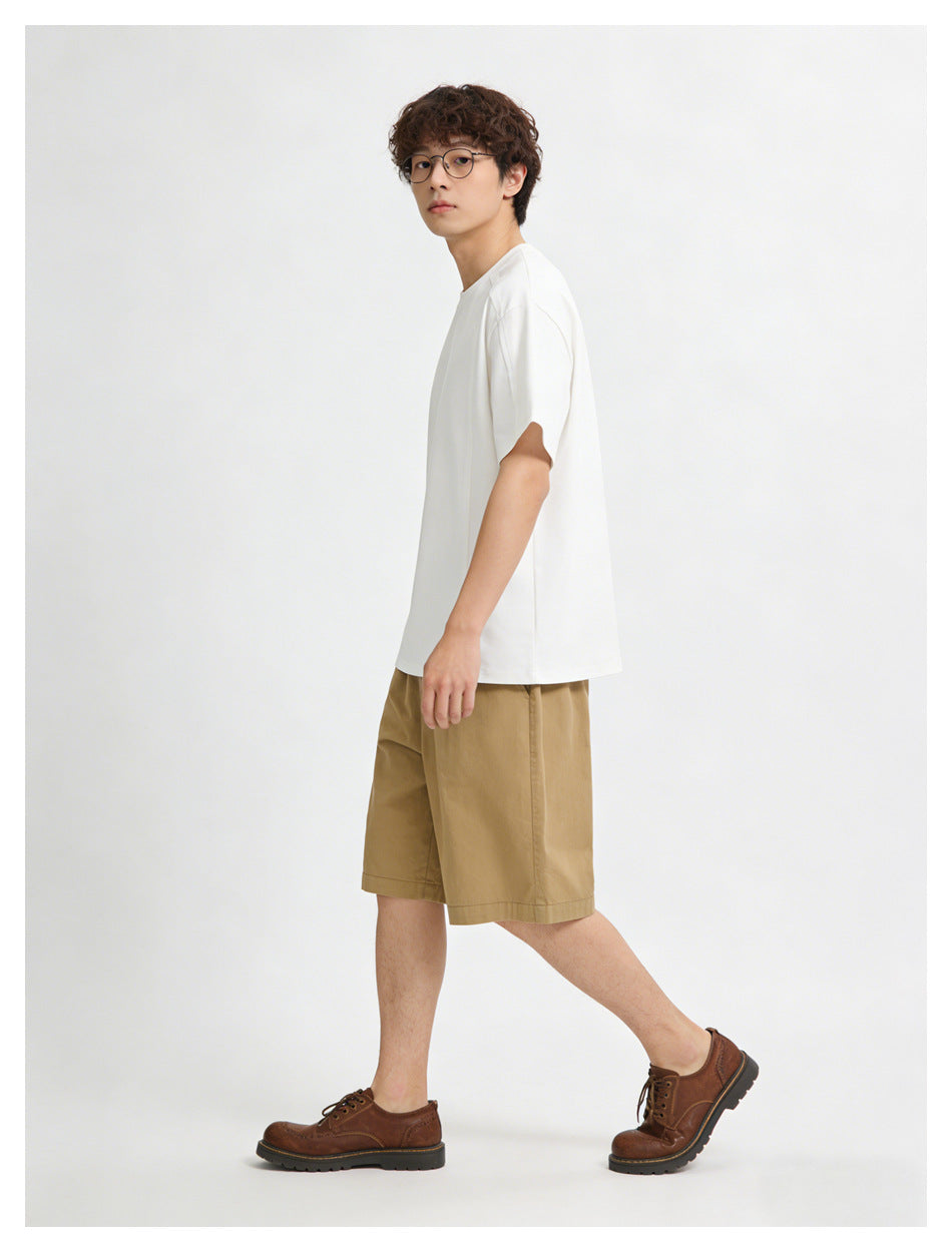 Model wearing a plain white short-sleeve T-shirt and tan shorts, shown in side view with brown lace-up shoes.