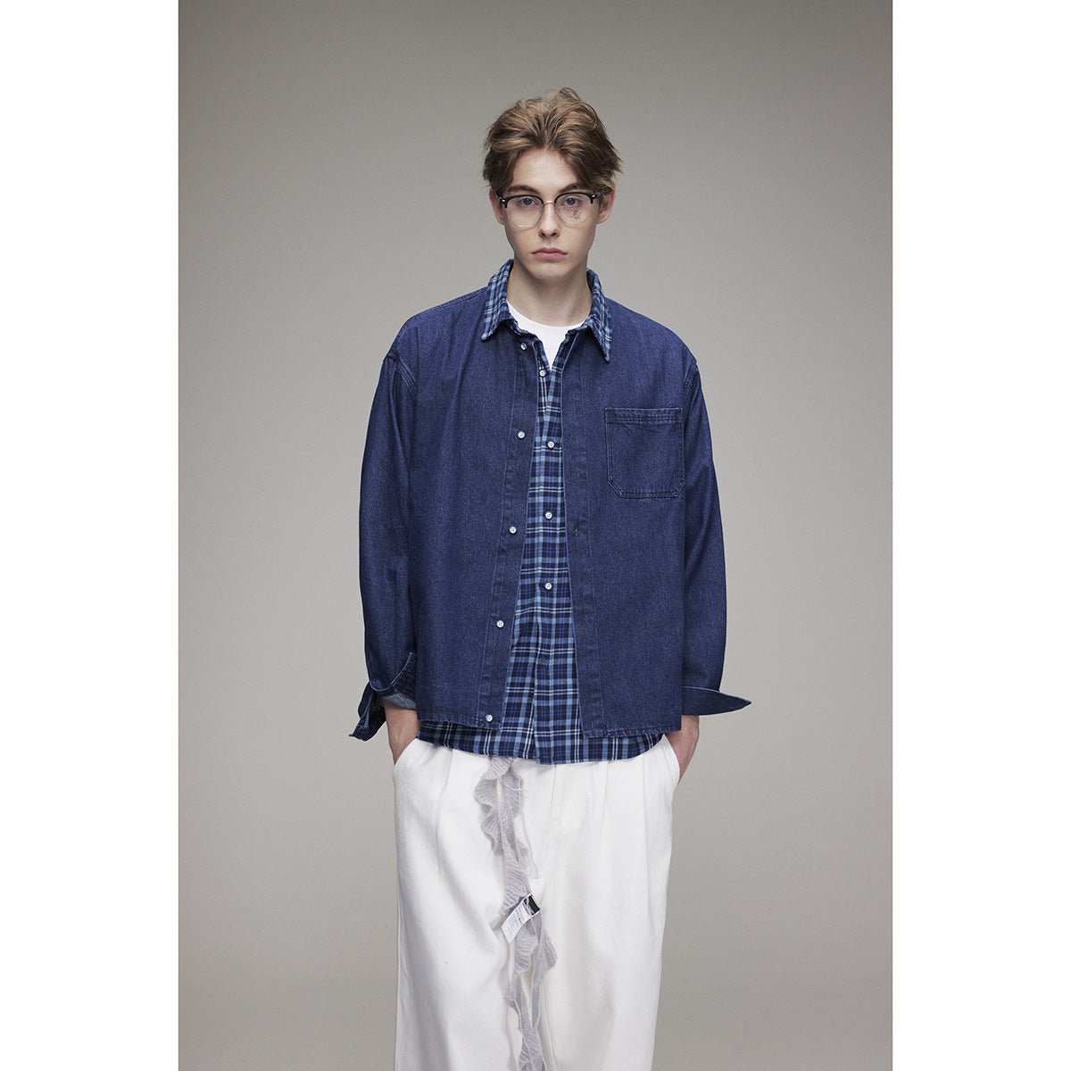 Model wearing a navy denim overshirt over a blue plaid shirt and loose white trousers, shown from the front.