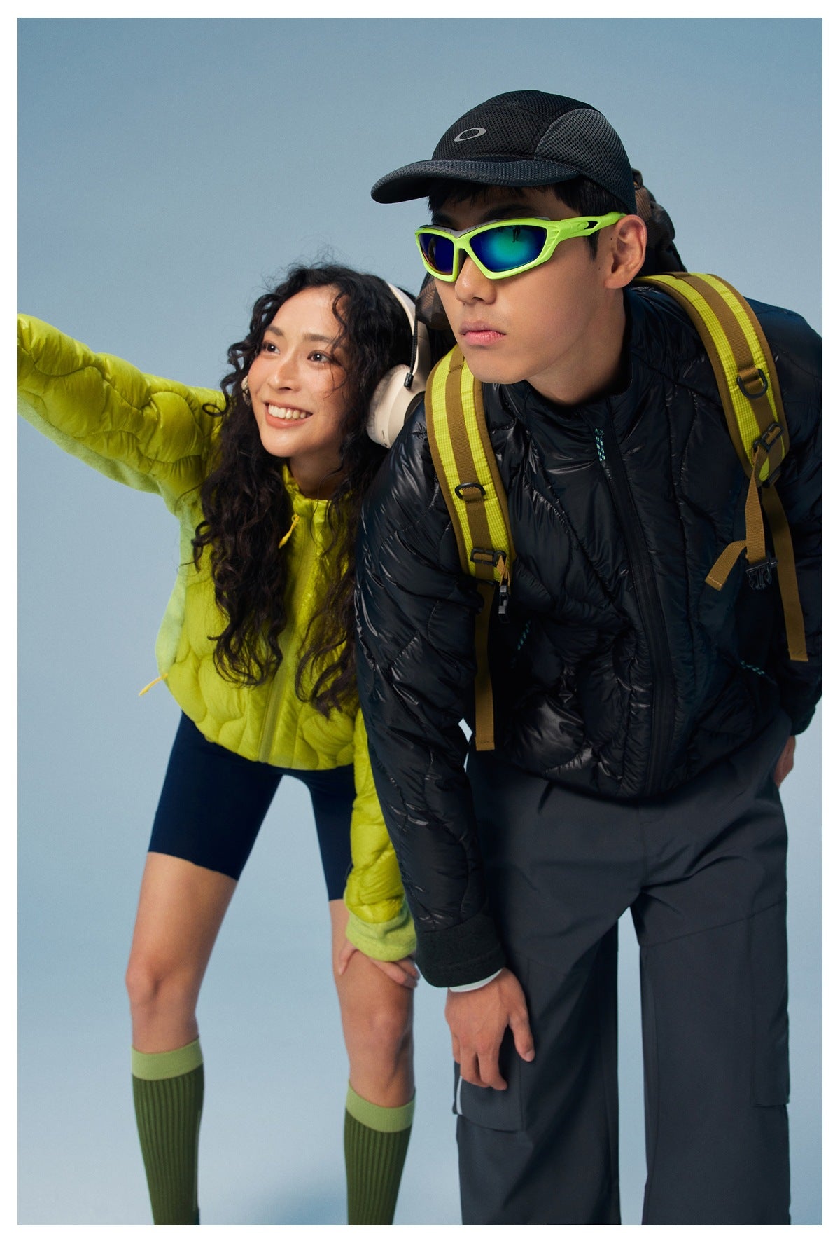 A man in a black quilted jacket and a woman in a lime quilted jacket lean forward together.