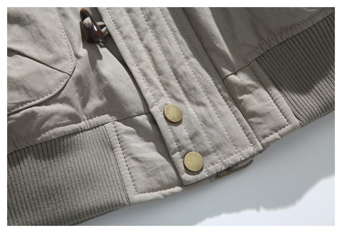 Close-up of a taupe jacket hem showing ribbed trim, brass-tone snaps and a toggle fastener.