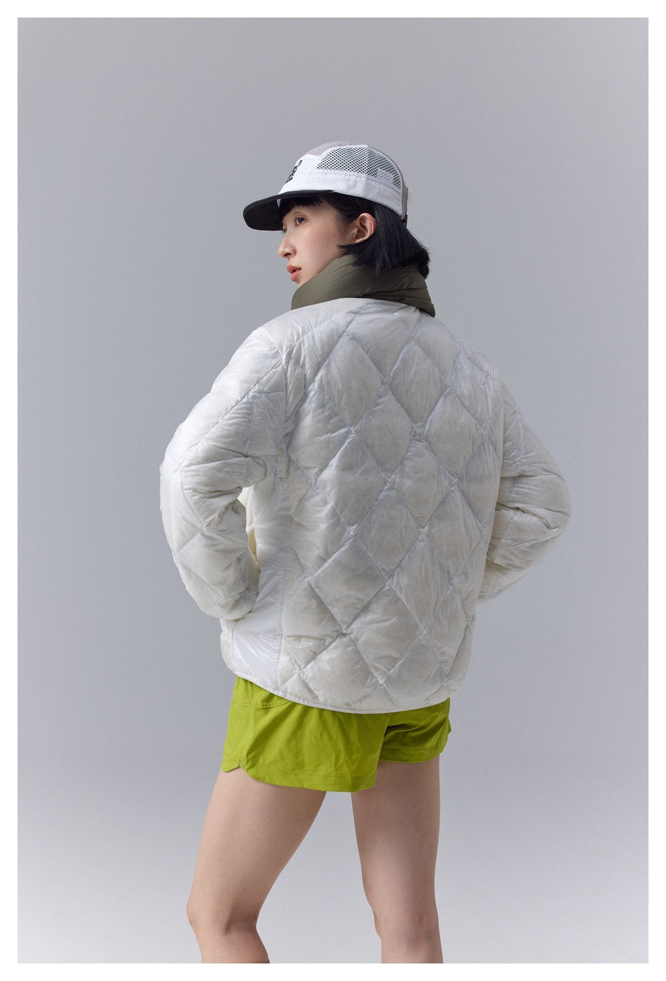 Model in a white diamond-quilted jacket and lime-green shorts, shown from behind with an olive scarf.