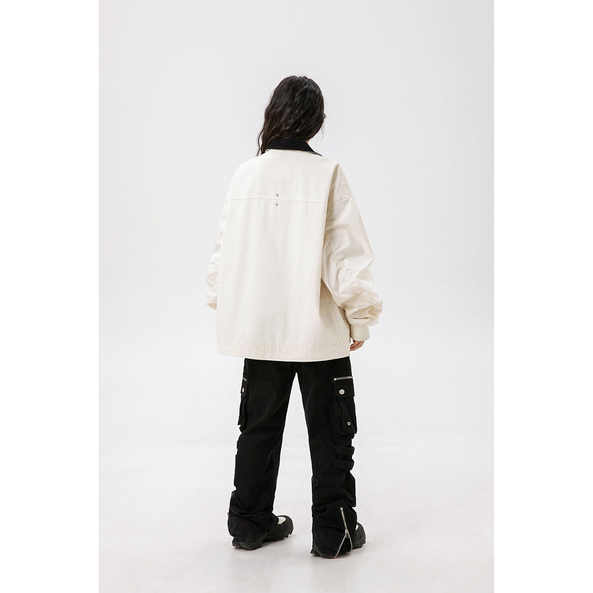 Rear view of a model wearing an ivory jacket with a black collar and black cargo pants.