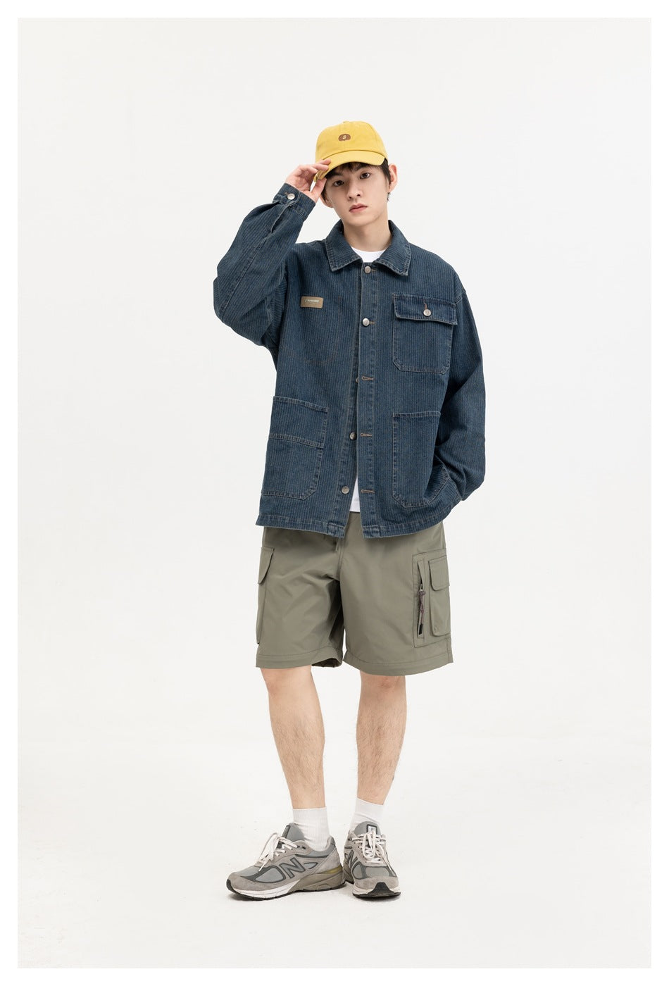A model poses in a dark blue denim chore jacket with multiple pockets and olive cargo shorts.
