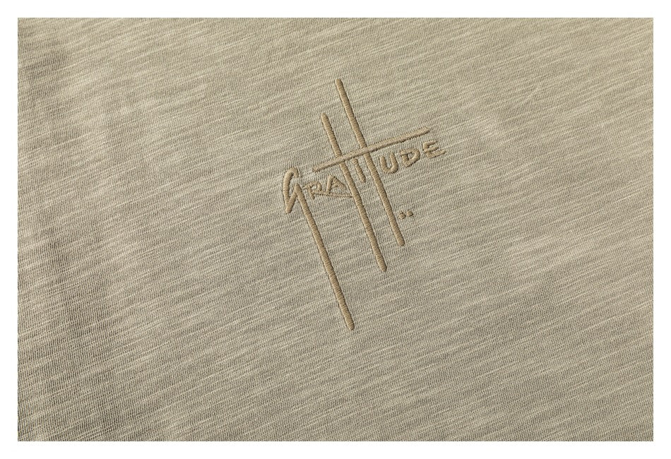 Close-up of the khaki shirt's small tonal embroidered chest emblem and lettering.