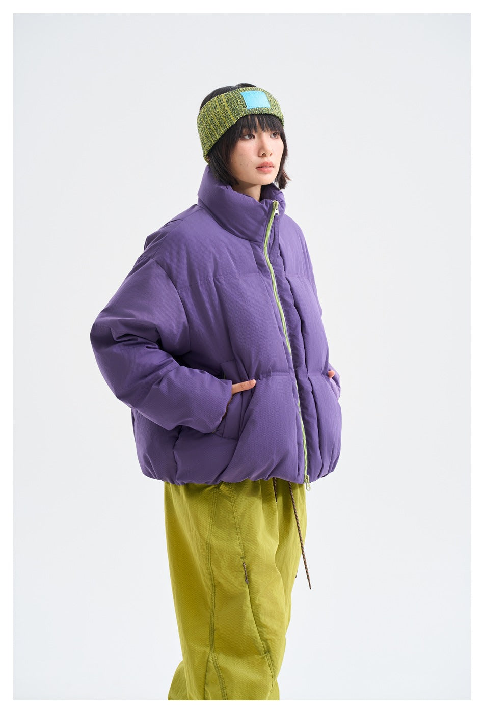 Closer view of a model wearing a purple puffer jacket with lime zipper, paired with lime trousers and a green knit headband.