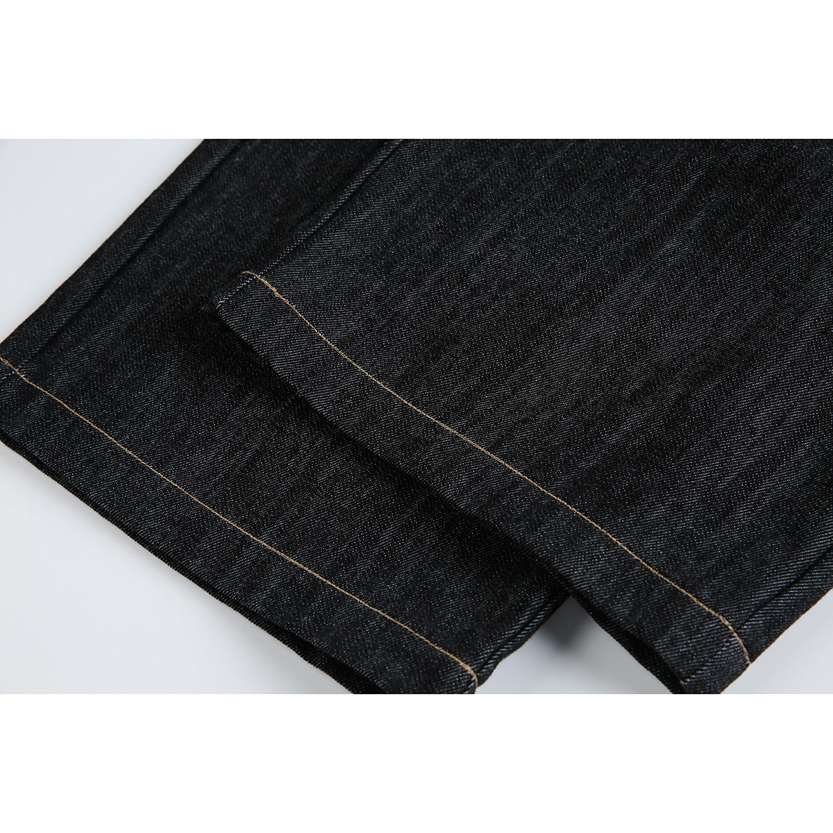 Close-up of dark indigo jeans showing a folded hem with tan contrast stitching.