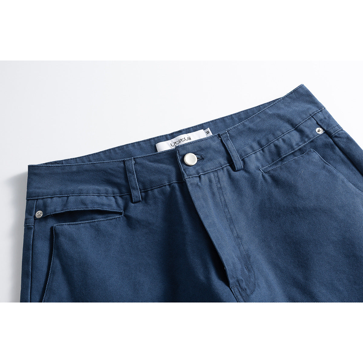 Close-up of dark blue trousers showing the waistband, button, belt loops and front pocket.