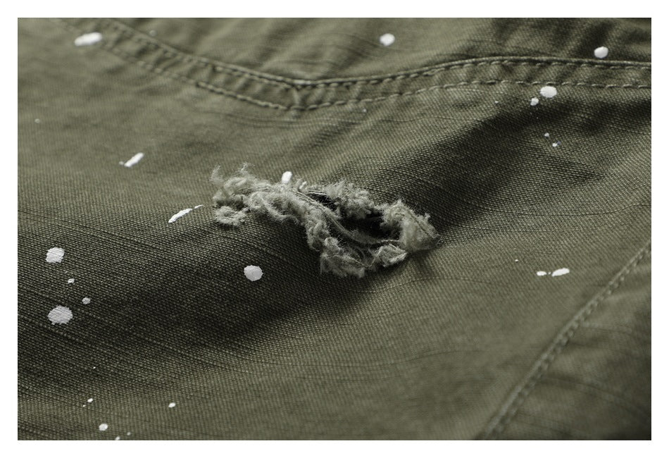 Close-up of a frayed tear and white paint splatters on olive pants fabric.