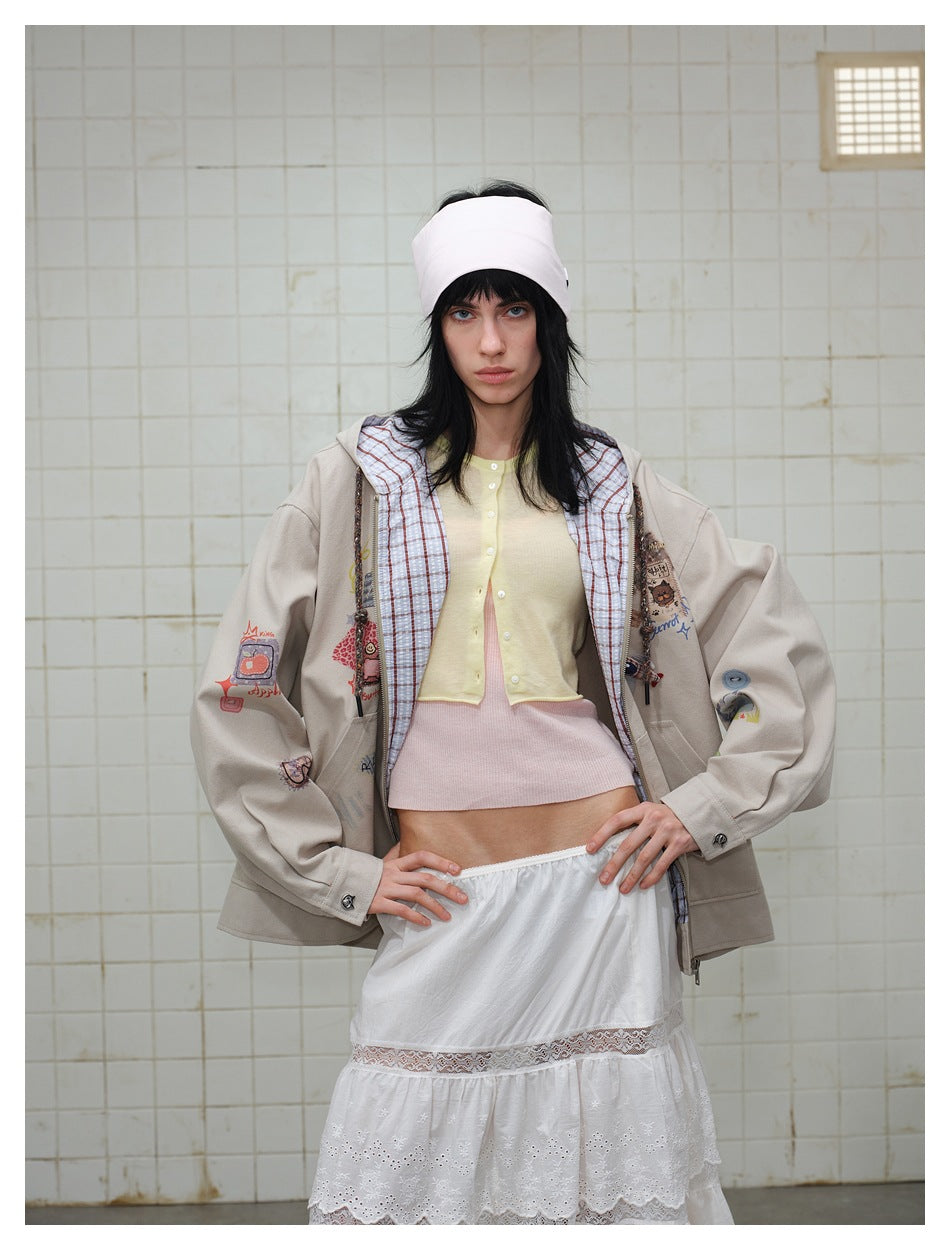 Model wearing a beige hooded jacket with colorful patches, a pale yellow cardigan, and a white lace skirt.