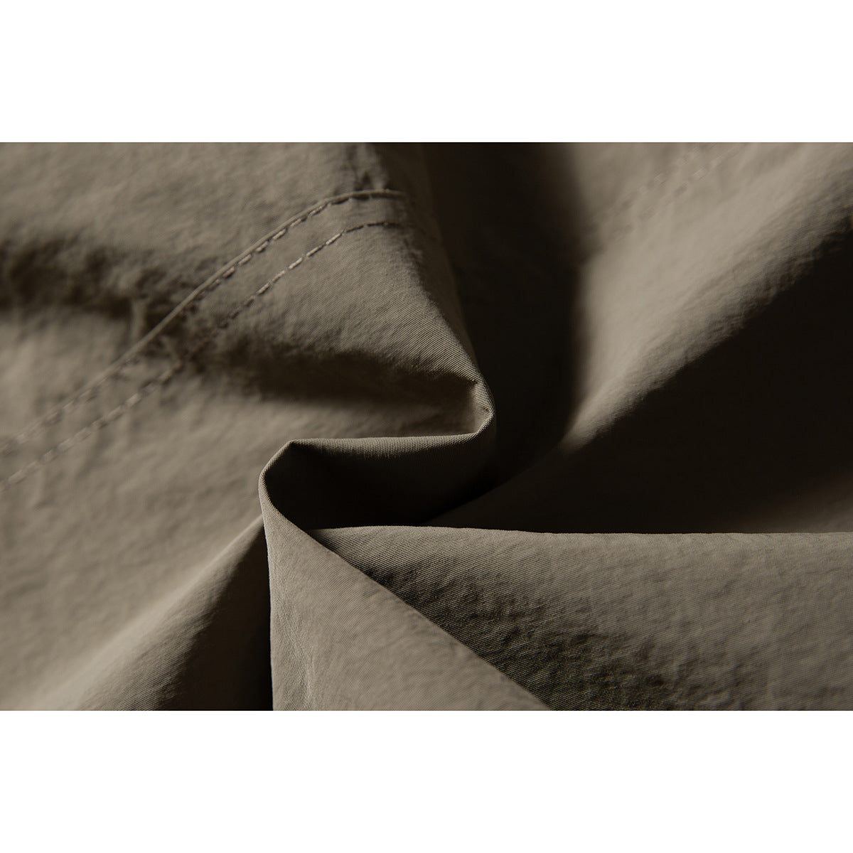 Macro view of olive-gray jacket fabric folds and curved double stitching.