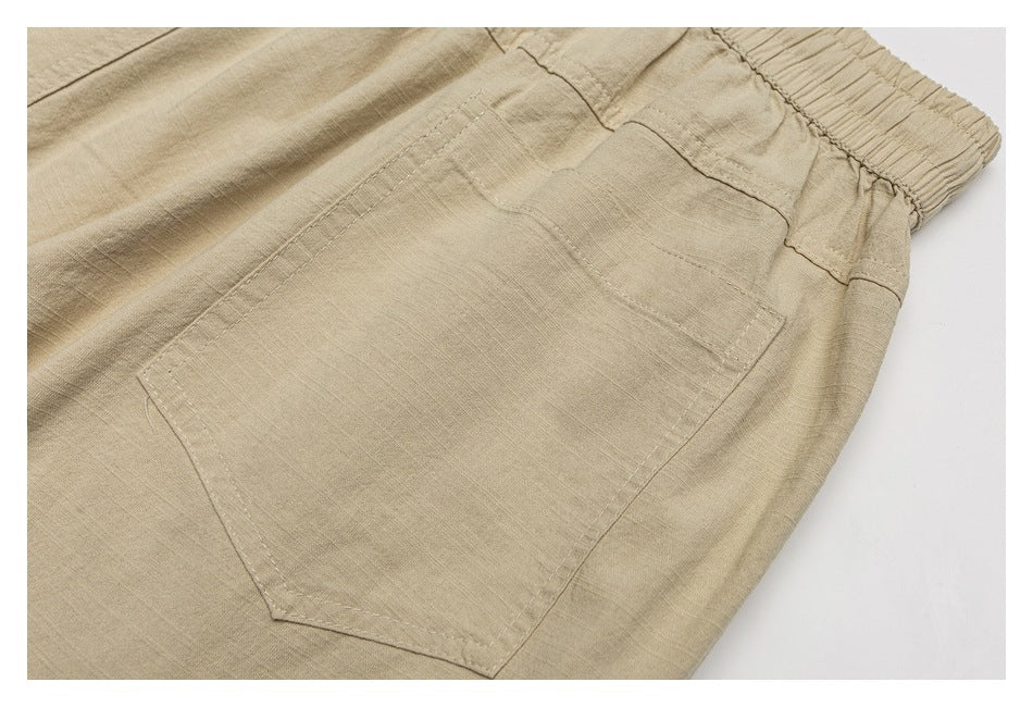 Close-up of beige trousers showing a stitched patch pocket and gathered elastic waistband.