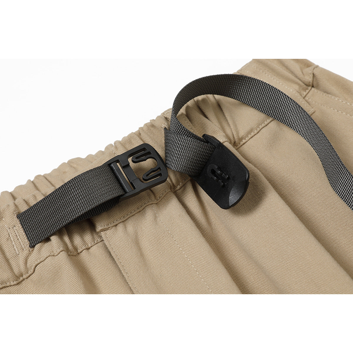 Close-up of tan pants with a black adjustable webbing belt and buckle at the elastic waistband.
