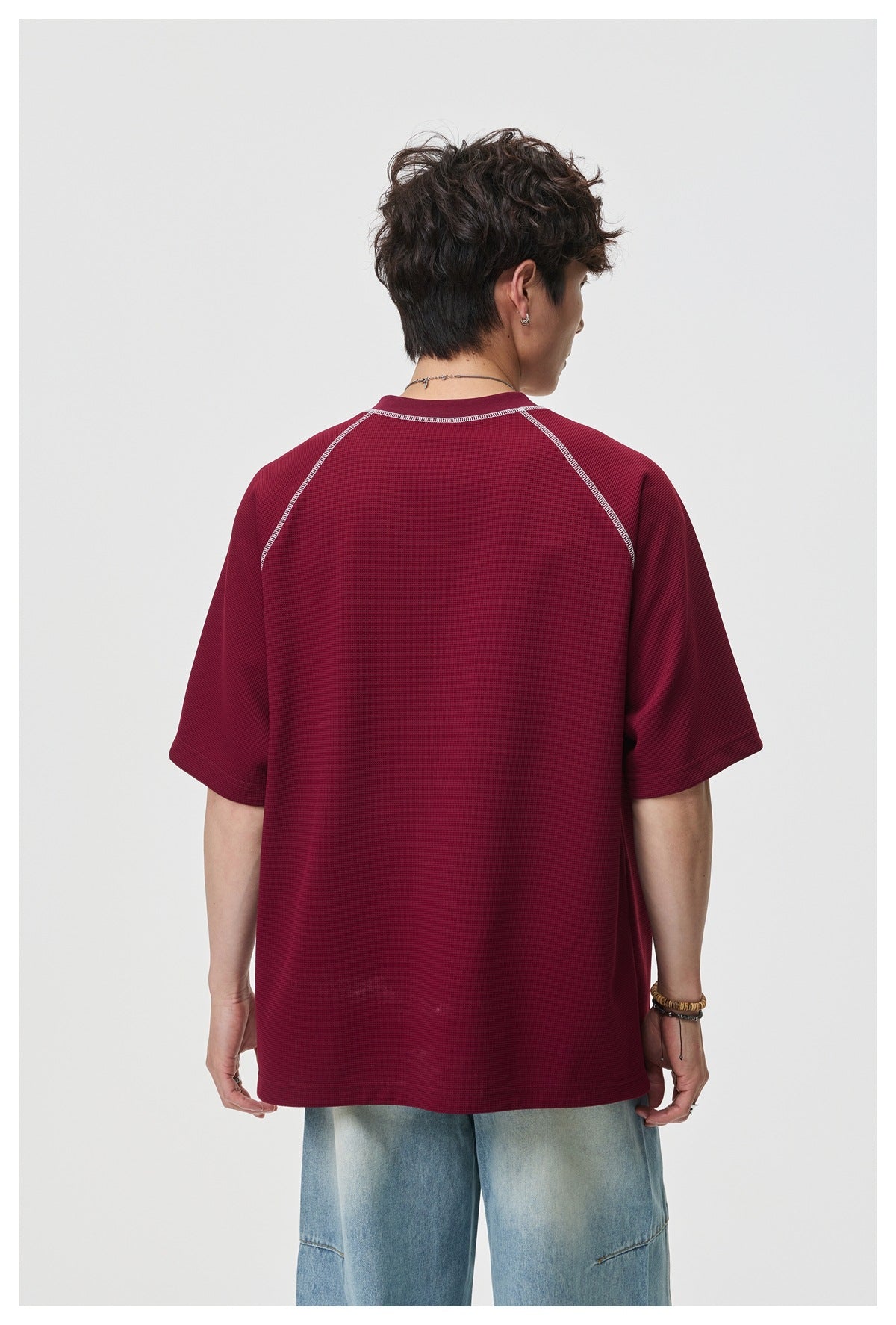 Rear view of a model wearing an oversized burgundy short-sleeve shirt with pale contrast raglan stitching.