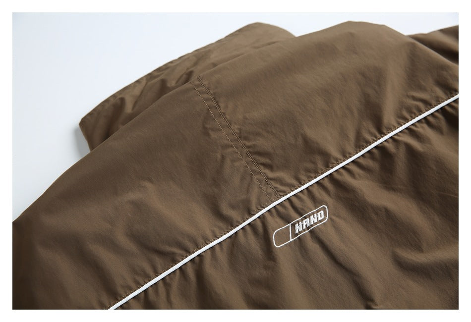 Brown jacket back detail with diagonal white piping and a small embroidered white emblem.