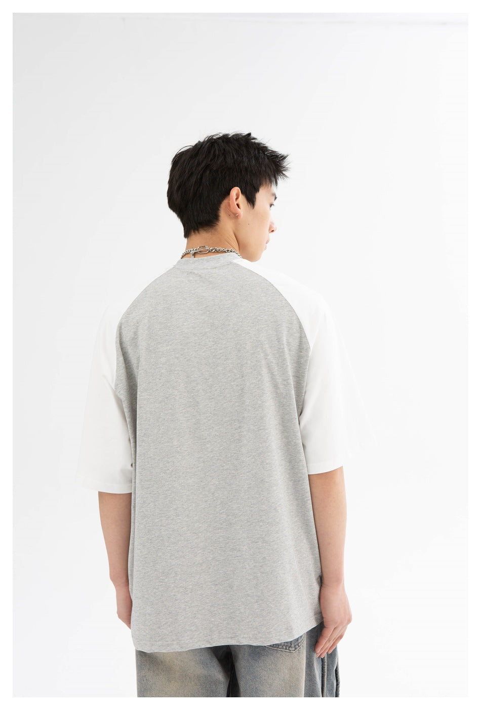 Back view of a model wearing a gray raglan T-shirt with white sleeves; the shirt has a plain back.