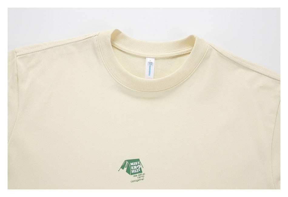 Close-up of a cream T-shirt’s crew neck and upper chest, showing a small green outdoor-themed graphic.