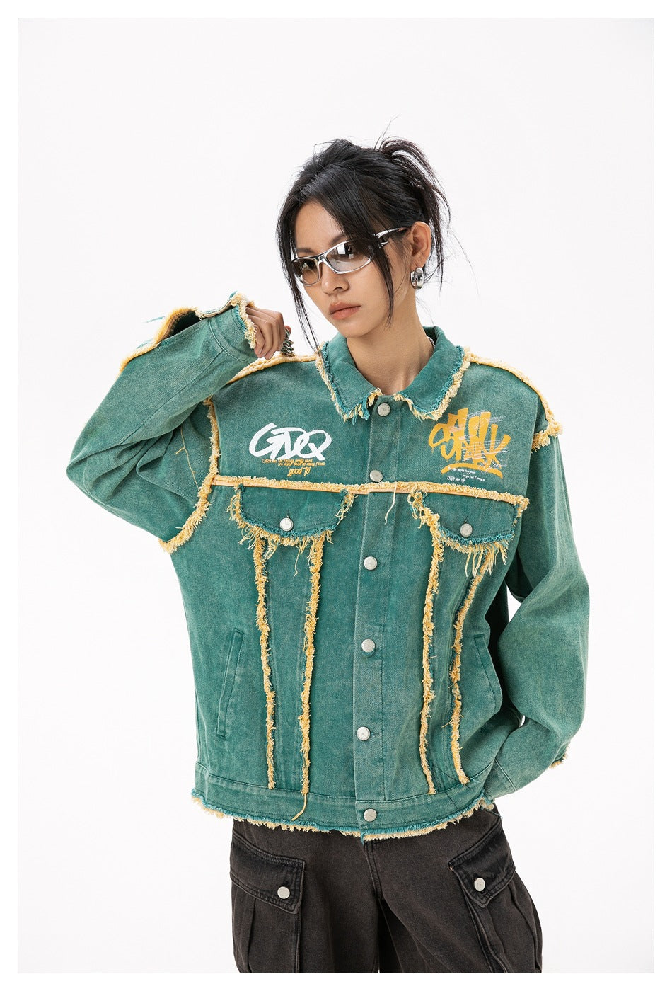 Closer front view of a model in a teal jacket with yellow frayed trim, printed chest graphics, and silver buttons.