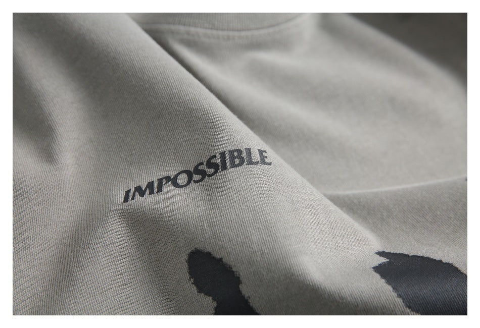 Close-up of the gray T-shirt fabric with part of the dark “IMPOSSIBLE” print visible.