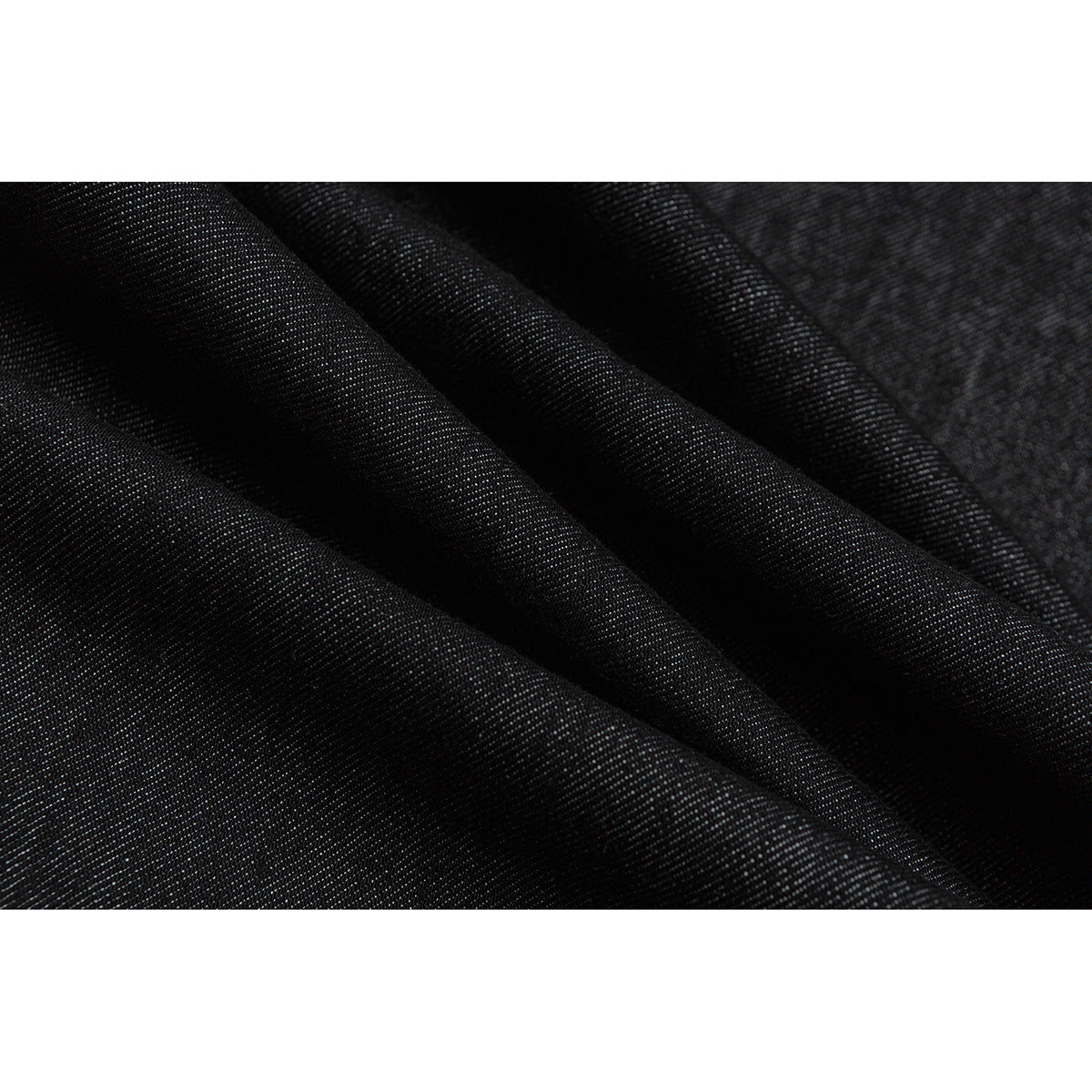 Macro view of dark black fabric arranged in soft folds, showing its fine diagonal texture.