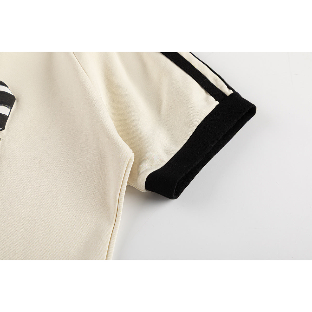 Close-up of a cream short sleeve with black edging and a narrow black shoulder stripe.