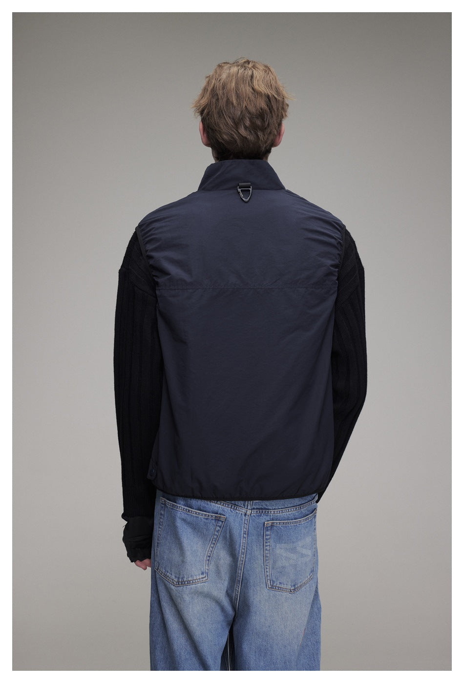 Back view of a model wearing a dark navy sleeveless vest with a high collar and small loop at the back neck.