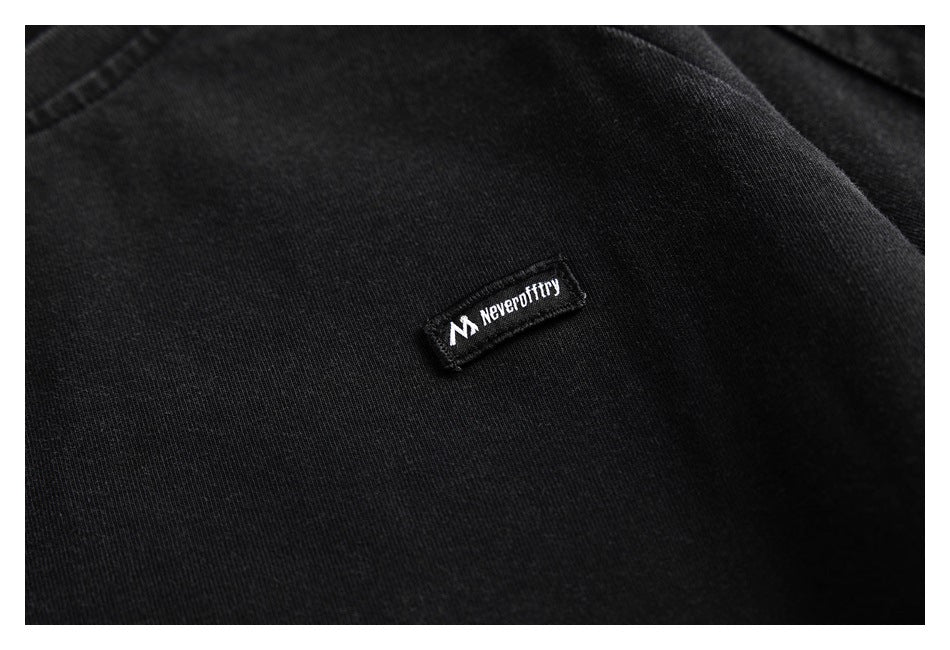 Close-up of a small white logo patch sewn onto black T-shirt fabric.
