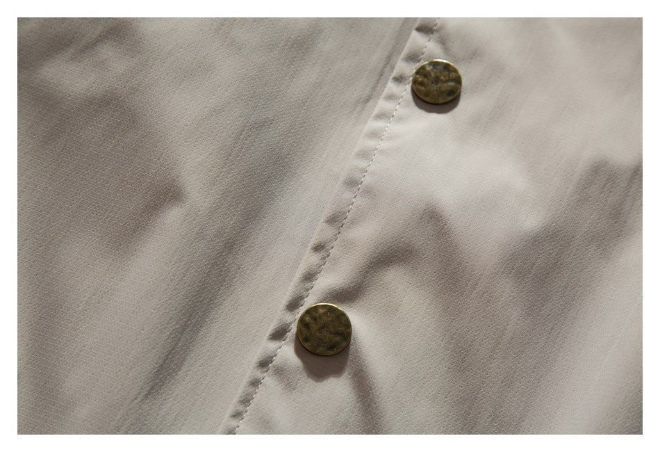 Close-up of the light taupe jacket fabric and two brass-tone buttons on a stitched placket.