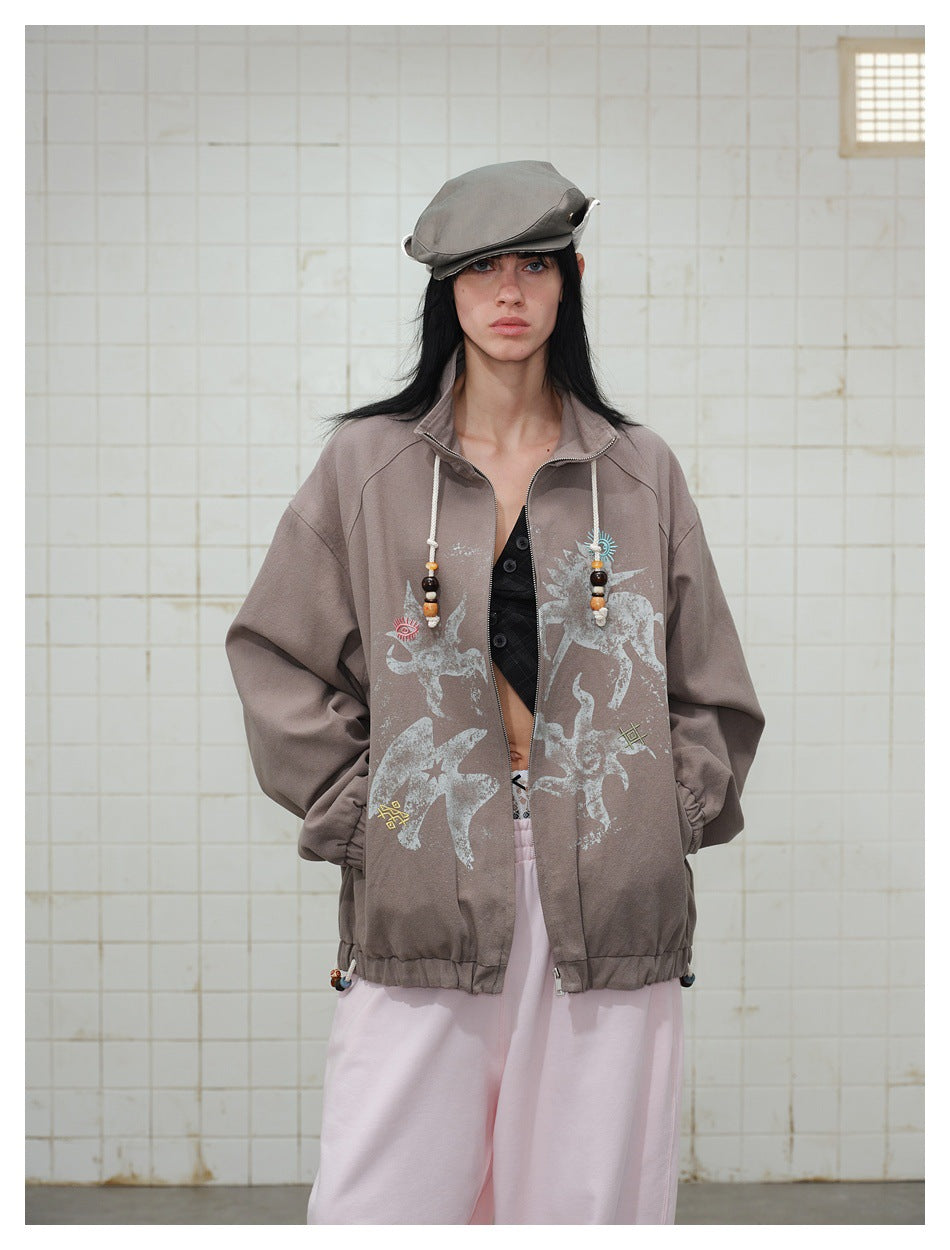 Front view of a model wearing an oversized taupe jacket with pale graphic prints and beaded drawstrings.