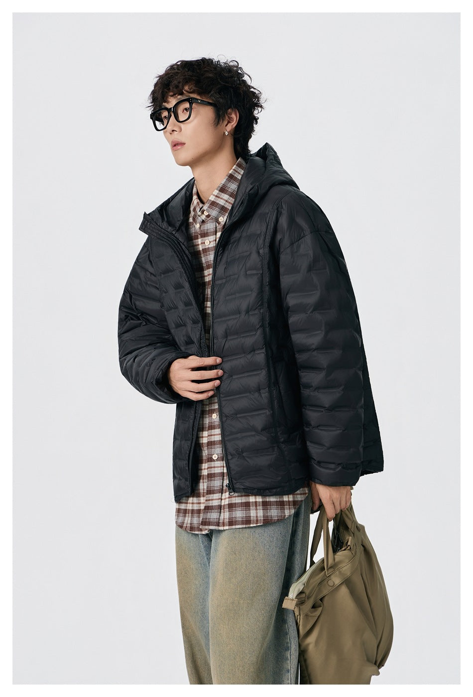 Closer view of a model wearing an open black quilted hooded puffer jacket over a plaid shirt.