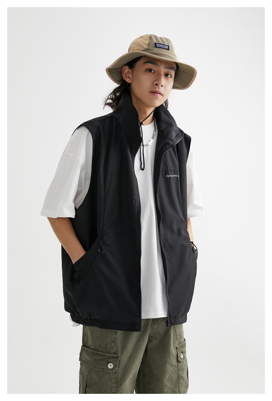 Model wearing an open black sleeveless vest with a high collar, front zipper, and drawcord pockets.