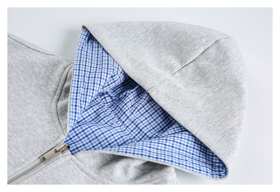 Close-up of a light gray hoodie hood with blue-and-white gingham lining and a metal zipper.