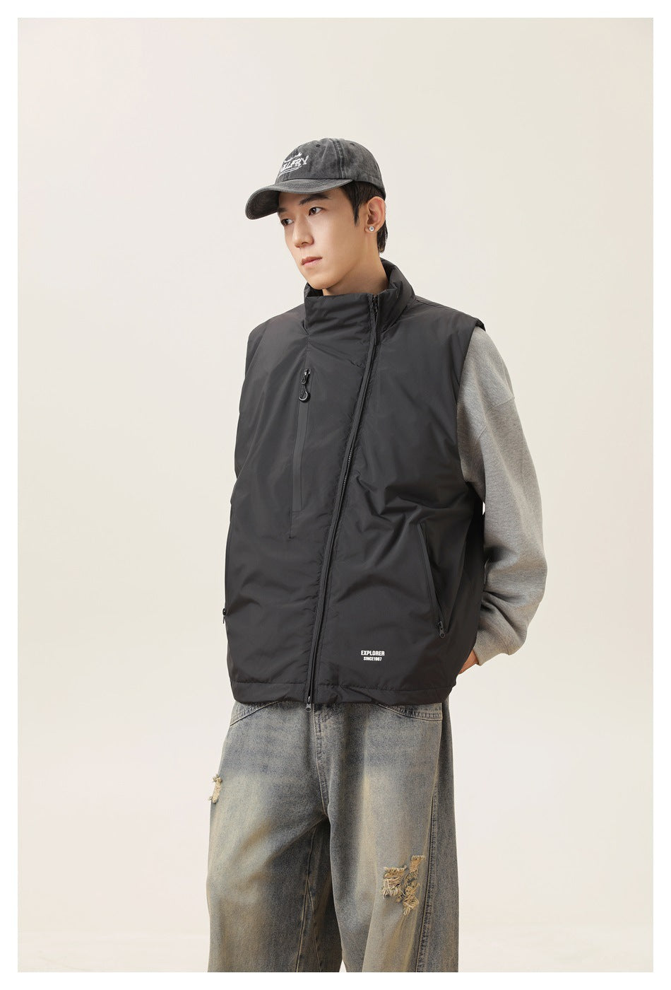 Three-quarter view of a model wearing a black high-collar zip vest over a gray sweatshirt.