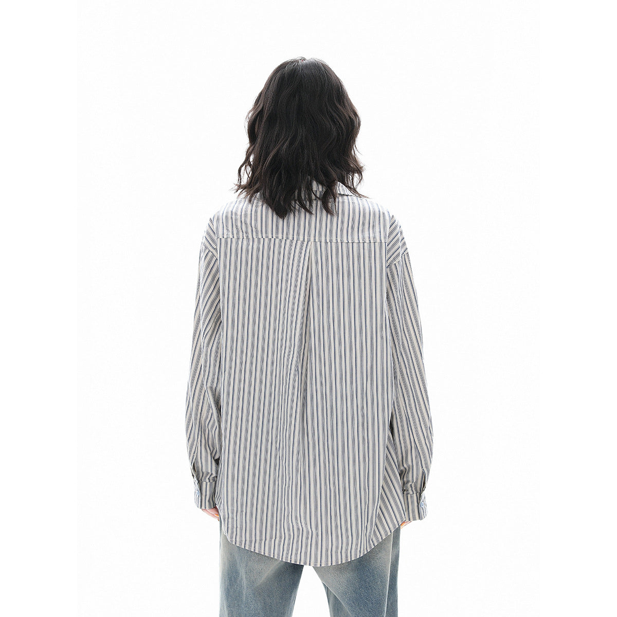 Back view of a model wearing an oversized blue-gray vertically striped shirt with a curved hem.