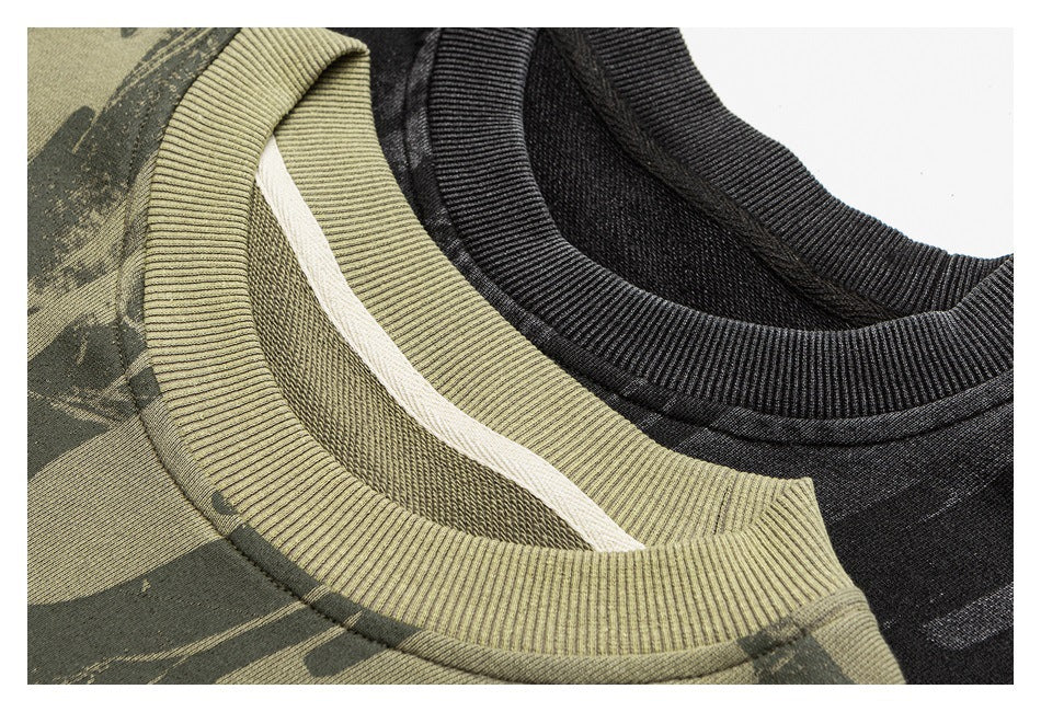 Close-up of ribbed crewneck collars on olive camouflage-print and charcoal graphic sweatshirts.
