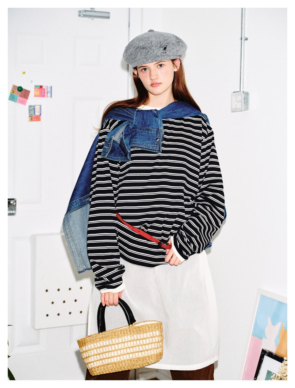 Model wearing navy and white striped long-sleeve top with denim shirt over shoulders, gray beret, red belt and straw bag