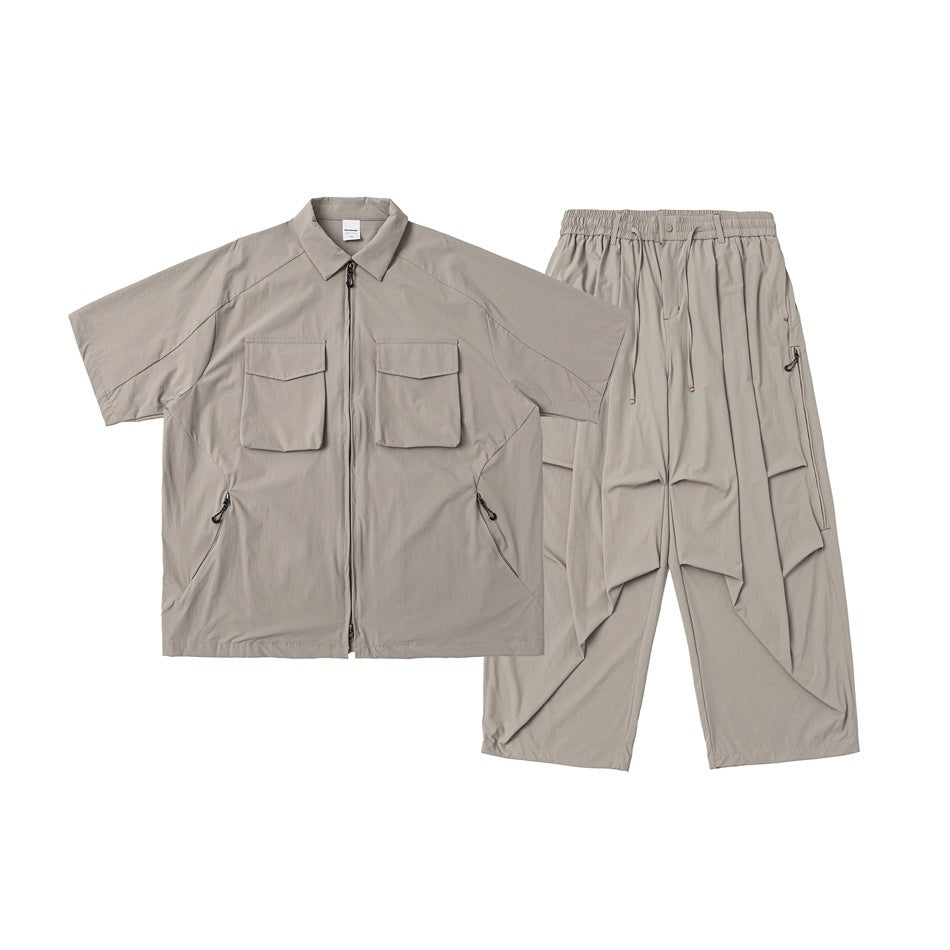 Light taupe two-piece set laid flat: short-sleeve zip shirt with flap pockets and relaxed drawstring trousers.