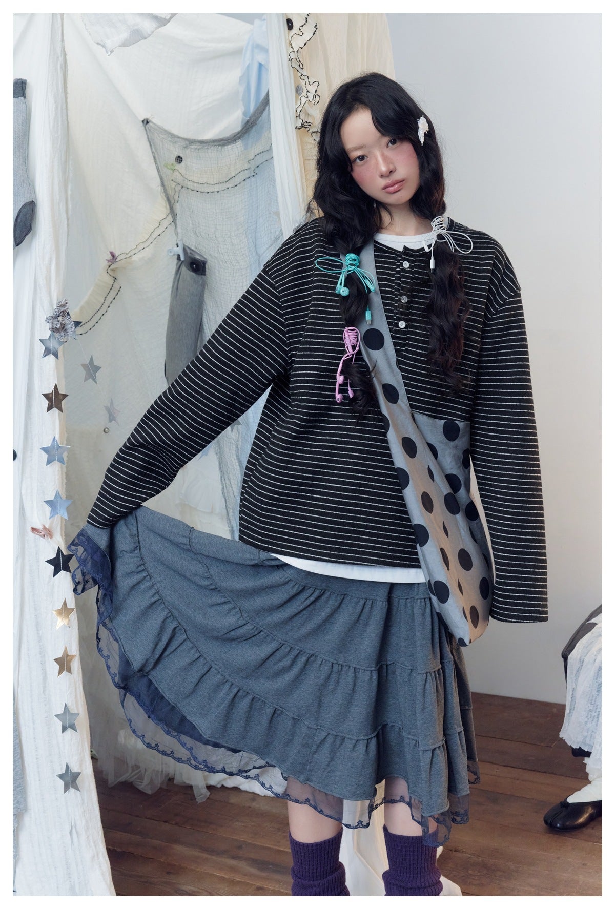 Model in a black-and-white striped top and charcoal tiered lace-hem skirt, holding the skirt out beside a gray polka-dot bag.