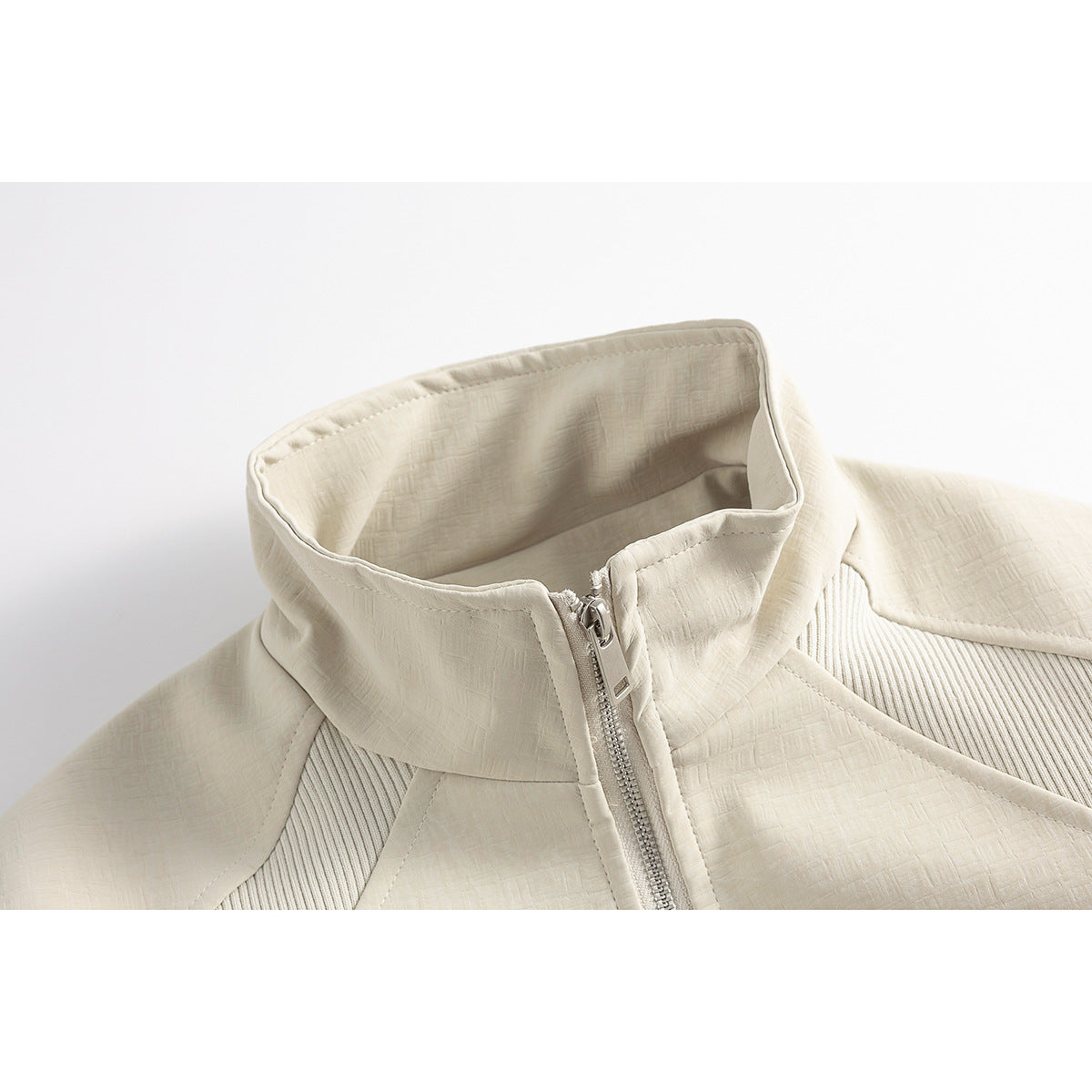 Close-up of an ivory jacket's stand collar, front zipper, and textured panels.